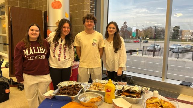 (Left to right) Romanian students Ellie Londono, ‘27, Irina Gut, ‘27, Marius Terenti, ‘26, and Bianca Cantemir, ‘28, stand by their table with dishes such as mititei, invartita, and cozonac.
